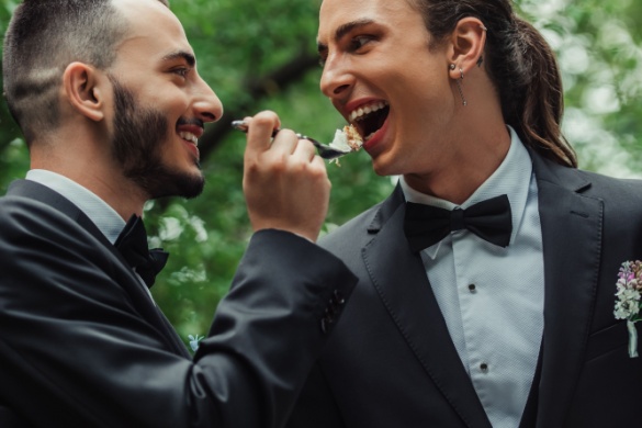 two grooms share a piece of cake at their wedding