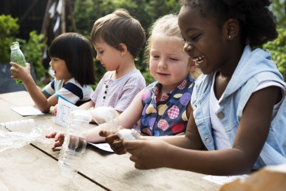a group of young children sit at a table outside making a craft